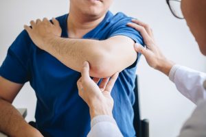 Doctor physiotherapist assisting a male patient while giving exercising treatment massaging the arm of patient in a physio room, rehabilitation physiotherapy concept